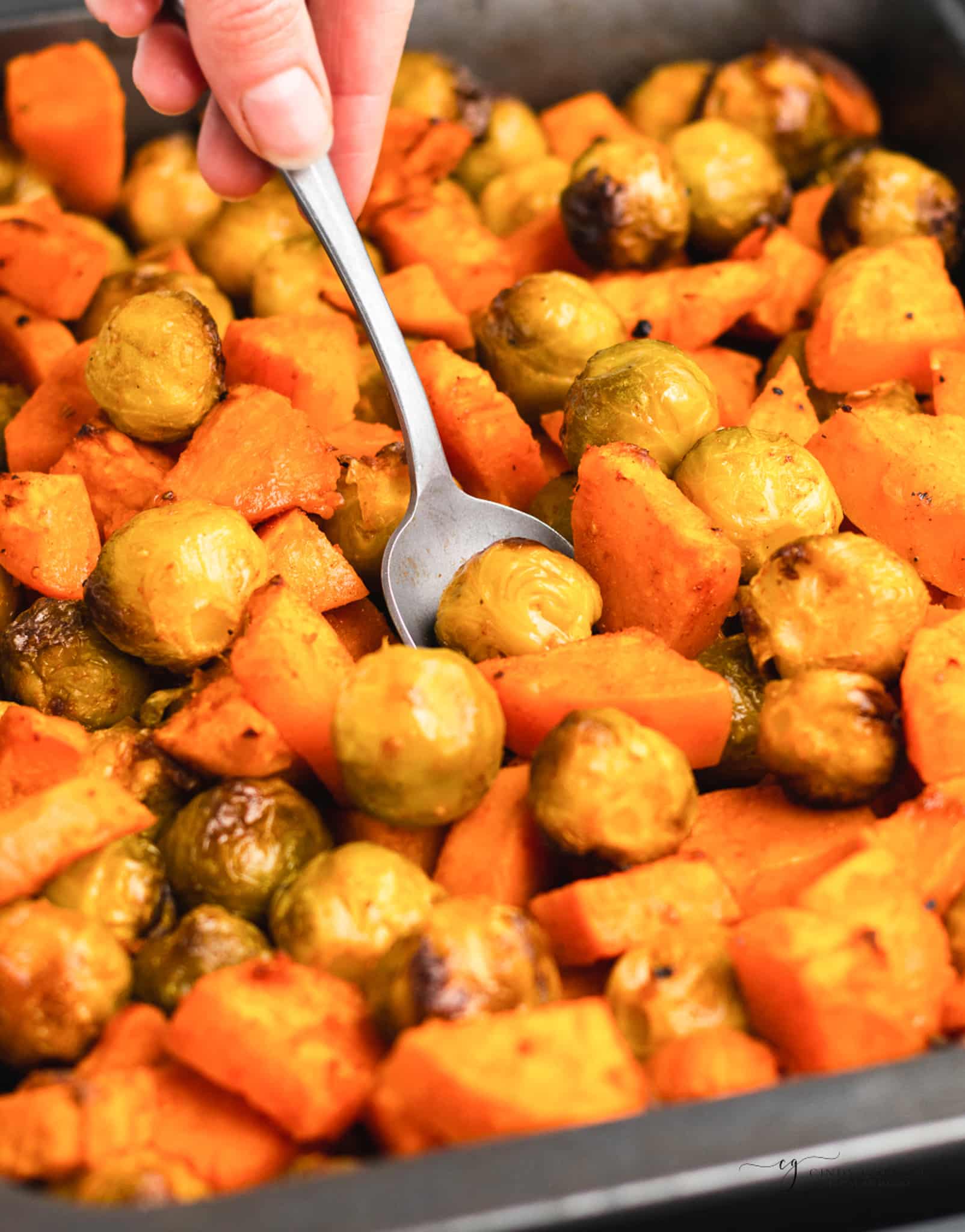 a pan of roasted sweet potatoes and brussel sprouts with a serving spoon in it.