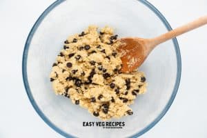 chocolate chip cookie dough in a glass bowl with a wooden spoon.