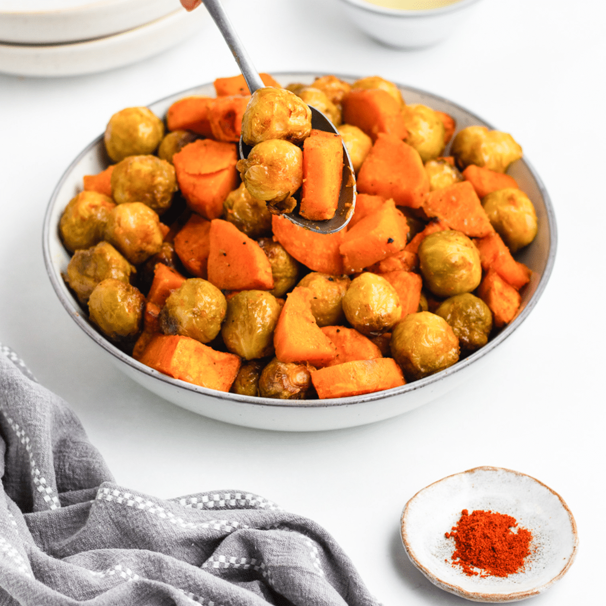 a bowl of roasted sweet potatoes and brussel sprouts with a serving spoon in it.
