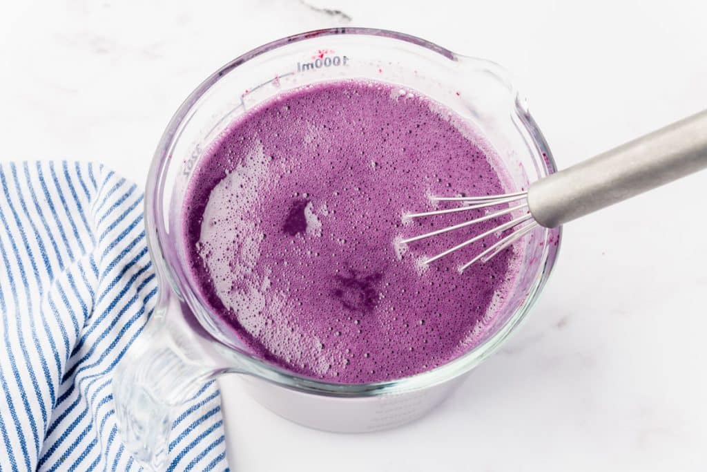 finished blueberry milk in a glass measuring cup with a whisk.