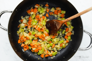 carrots, onion, celery sauteed in a pan with a wooden spoon.
