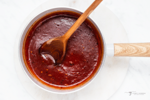 a small saucepan with dark red sauce, stirred with a wooden spoon.