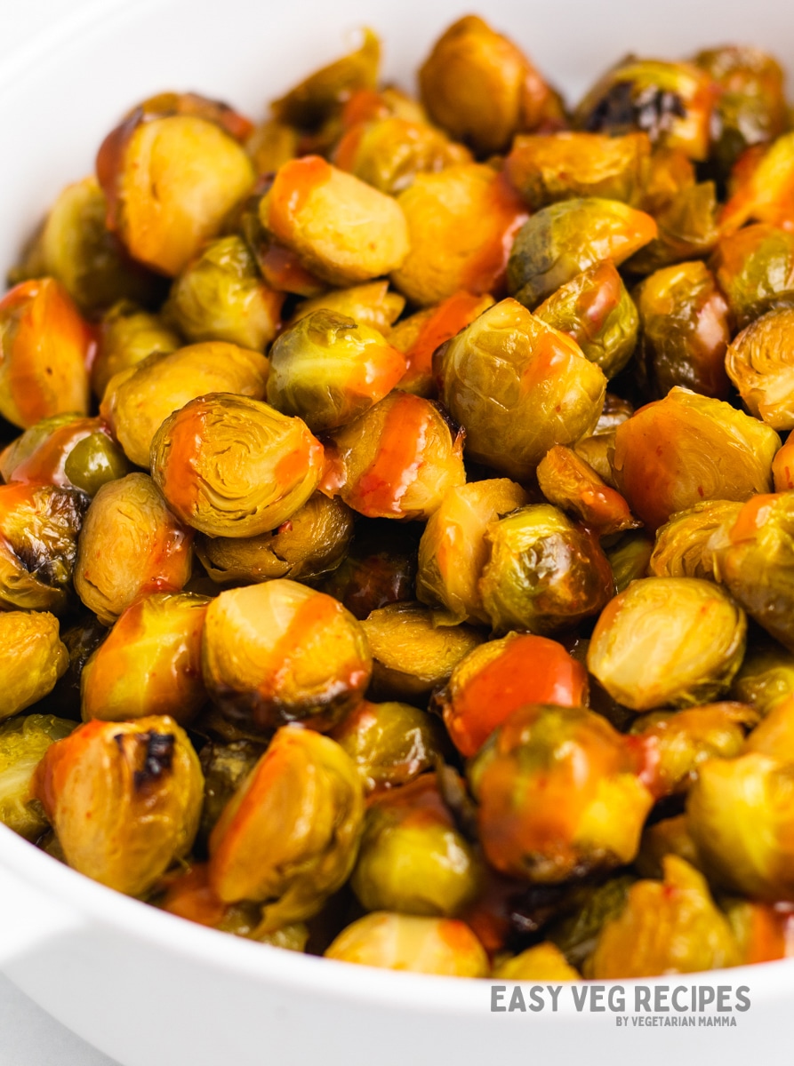 a white serving bowl filled with honey sriracha brussel sprouts.