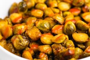 a white serving bowl filled with honey sriracha brussel sprouts.