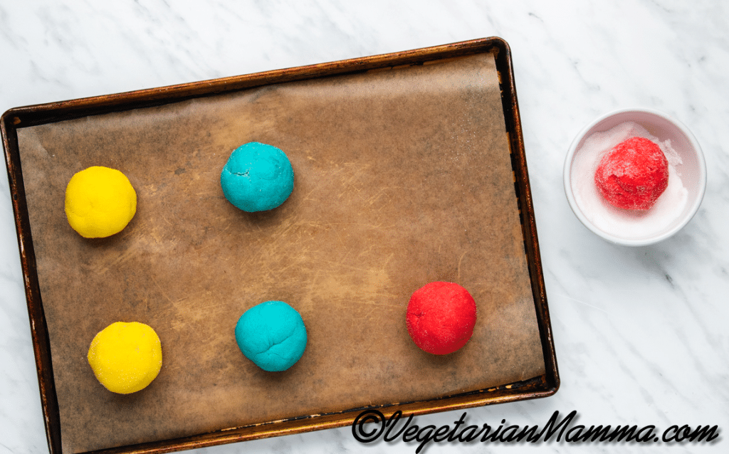 Roll the colored mixtures into large balls and dip them in the extra sugar. Each color should make about 4 balls. Place the cookie balls on the prepared baking sheets.