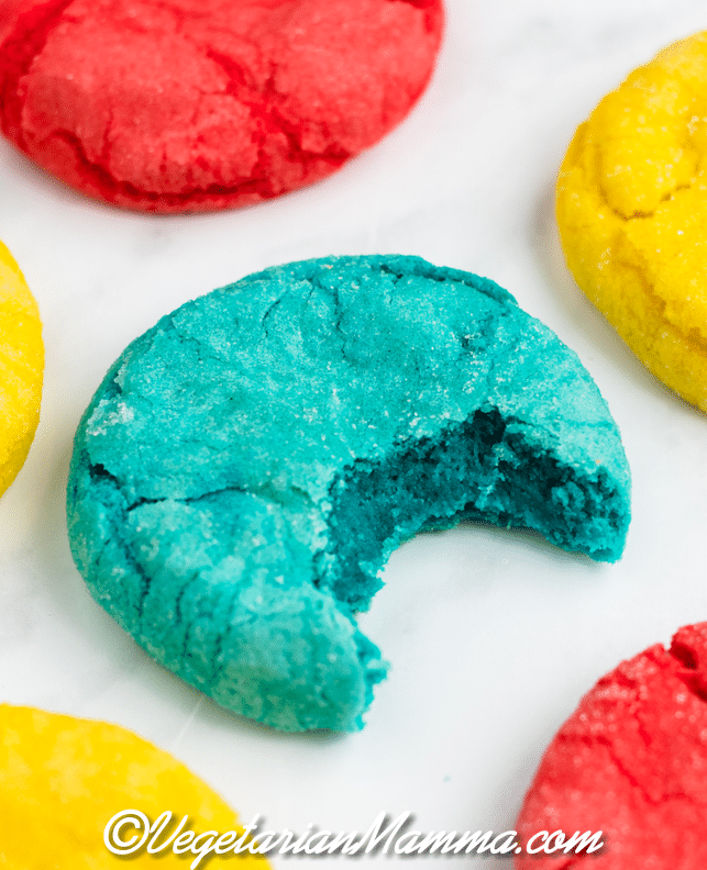 colorful Mexican sugar cookies. One blue one has a bite taken, showing the soft inside. 
