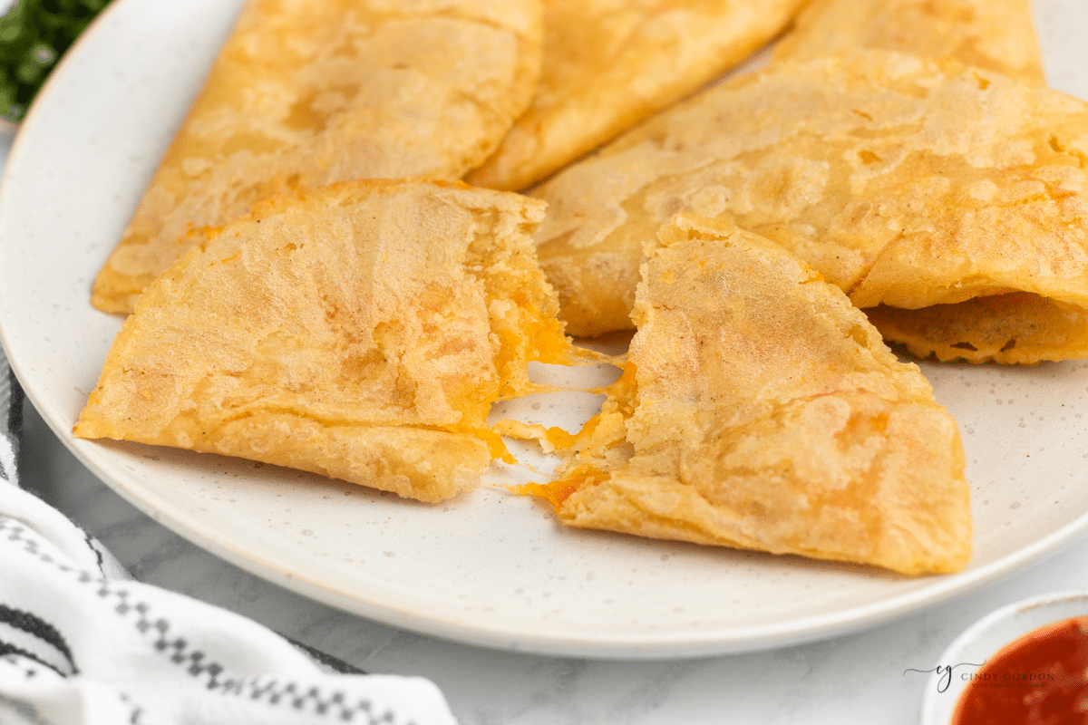 closeup of a plate of quesadillas fritas. One is torn in half to show melty cheese. 