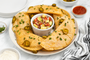 a round platter of fried quesadillas, with a cup of fresh salsa in the center.