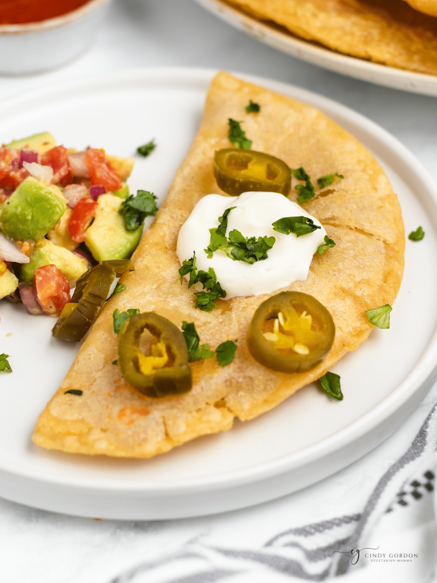 a folded quesadilla fritas topped with sour cream and pickled jalapenos next to a tomato avocado salad. 