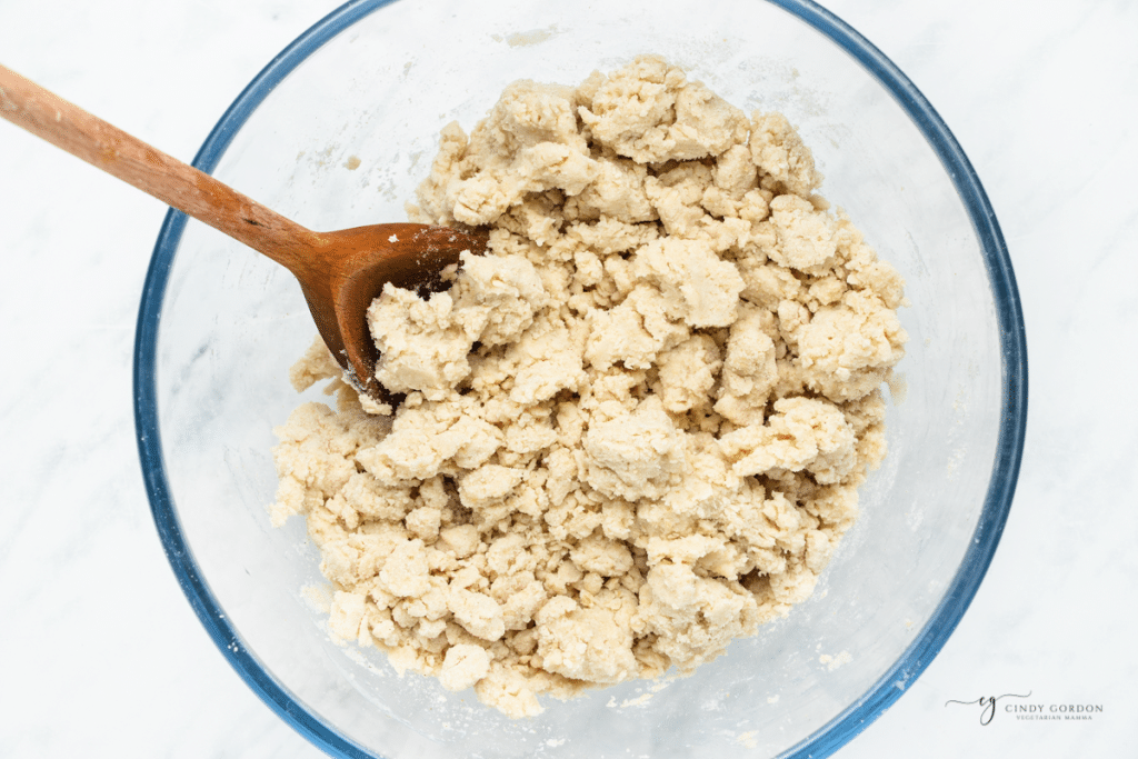 masa harina tortilla dough being mixed in a bowl with a wooden spoon.