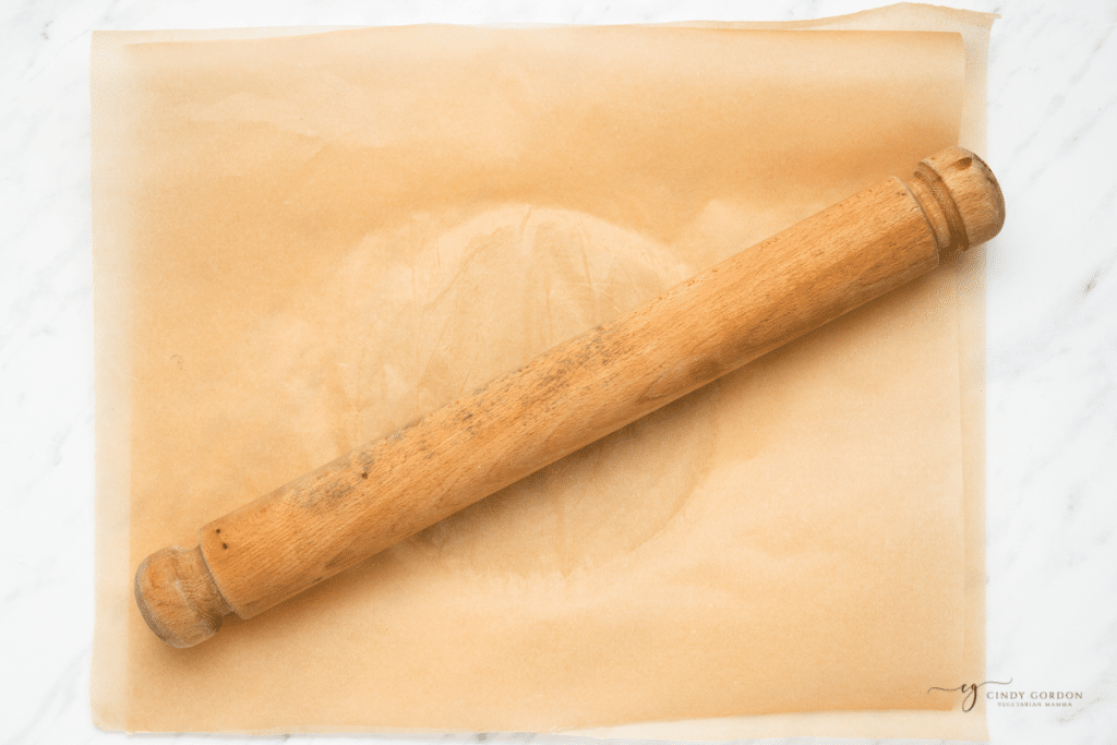 a wooden rolling pin making tortillas between parchment paper sheets.