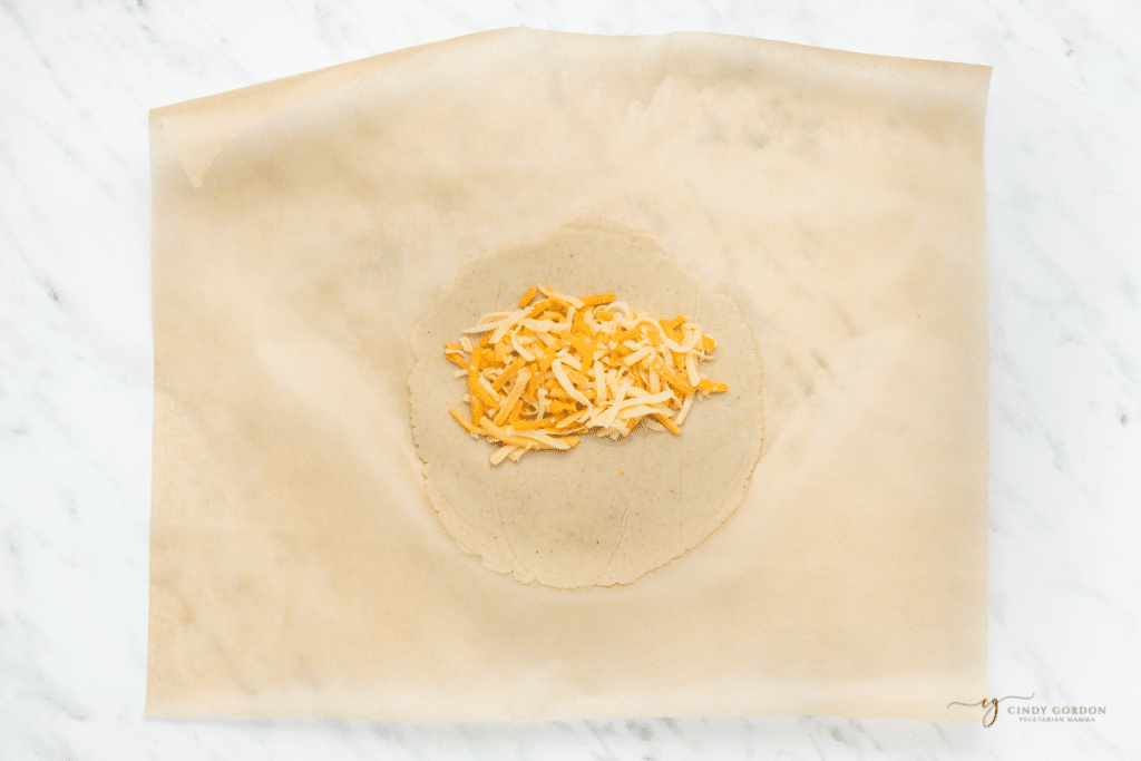 cheese on a tortilla that is on a piece of parchment paper.