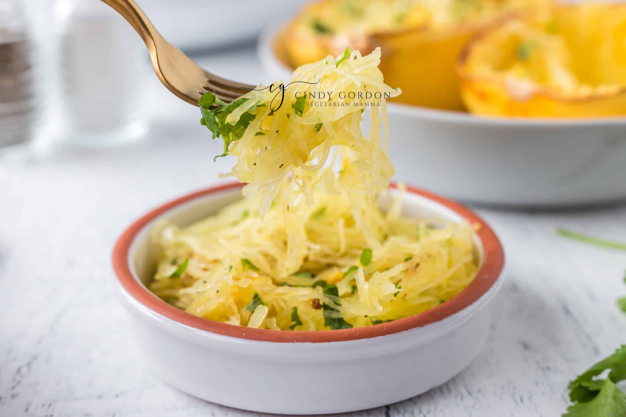 A bowl of cooked air fried spaghetti squash. A fork is holding up flaky strings of squash.