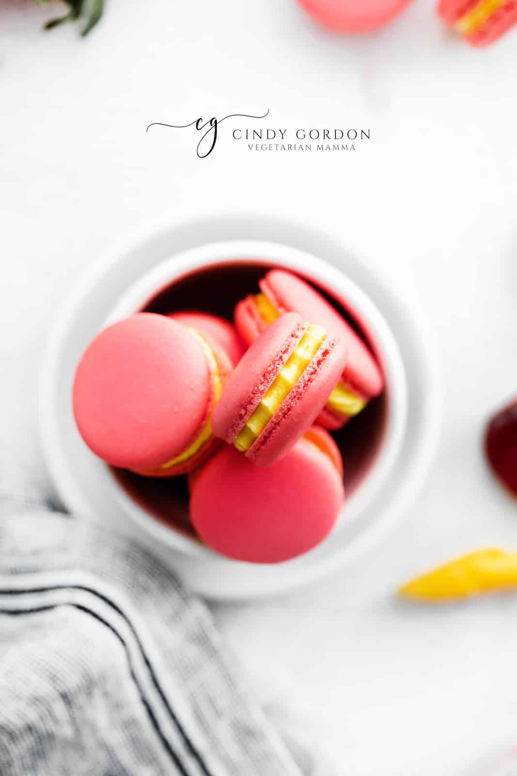 a small bowl of pink and yellow strawberry macarons, viewed from above.