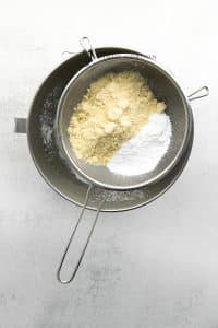 Almond flour sifted over a bowl of egg whites.