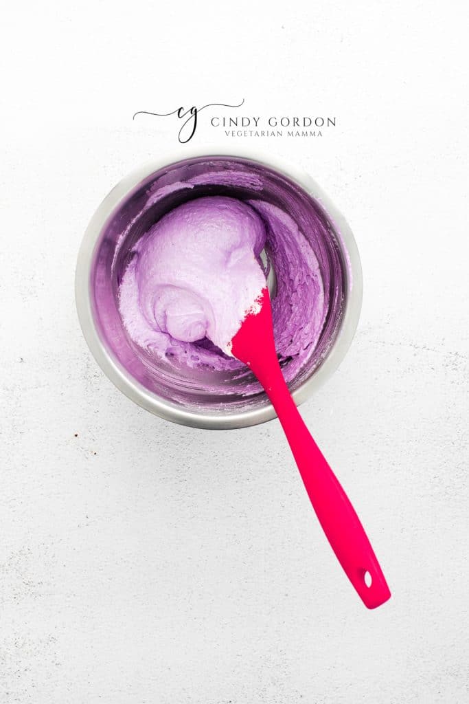 a bowl of purple macaron batter, stirred with a red spoon