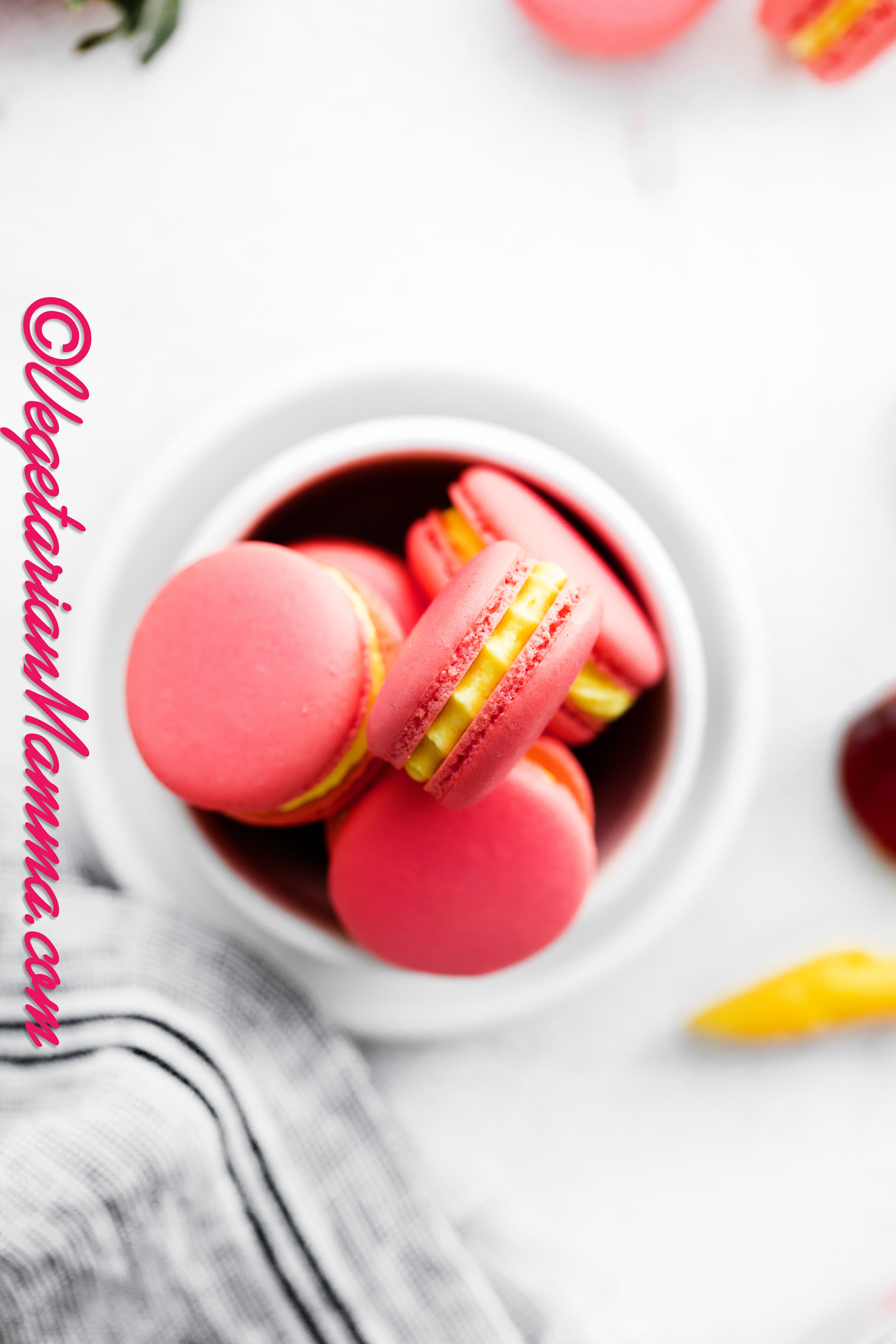 a small bowl of pink and yellow strawberry macarons, viewed from above.