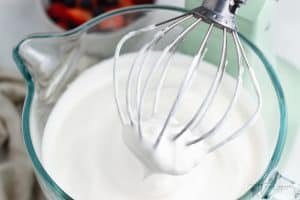 a glass mixing bowl of a stand mixer filled with fluffy aquafaba whipped cream.