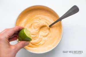 A hand squeezing half a lime into a bowl of seasoned sour cream.
