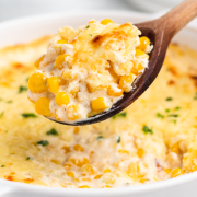 A round dish of cream cheese corn casserole with a wooden spoon serving it.