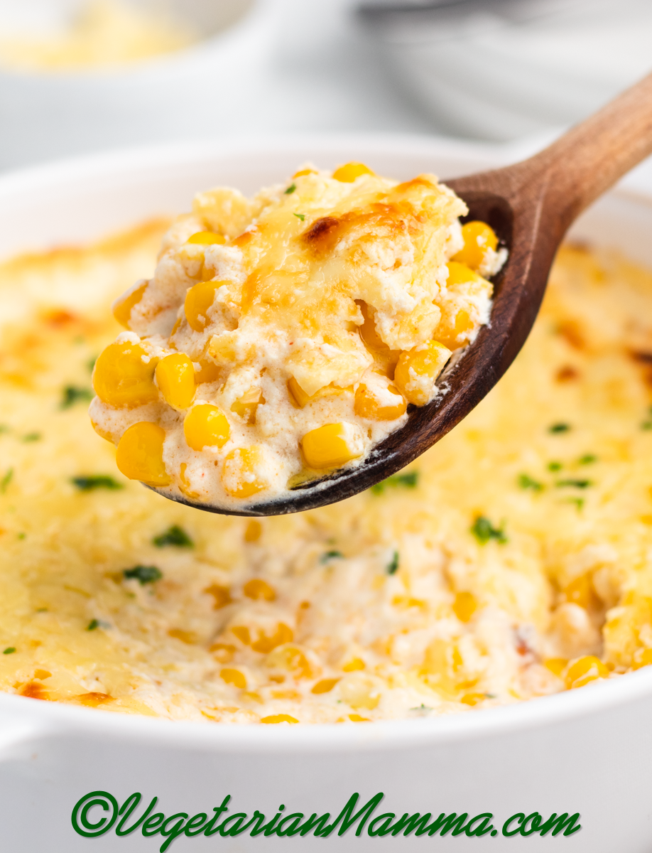 A round dish of cream cheese corn casserole with a wooden spoon serving it. 