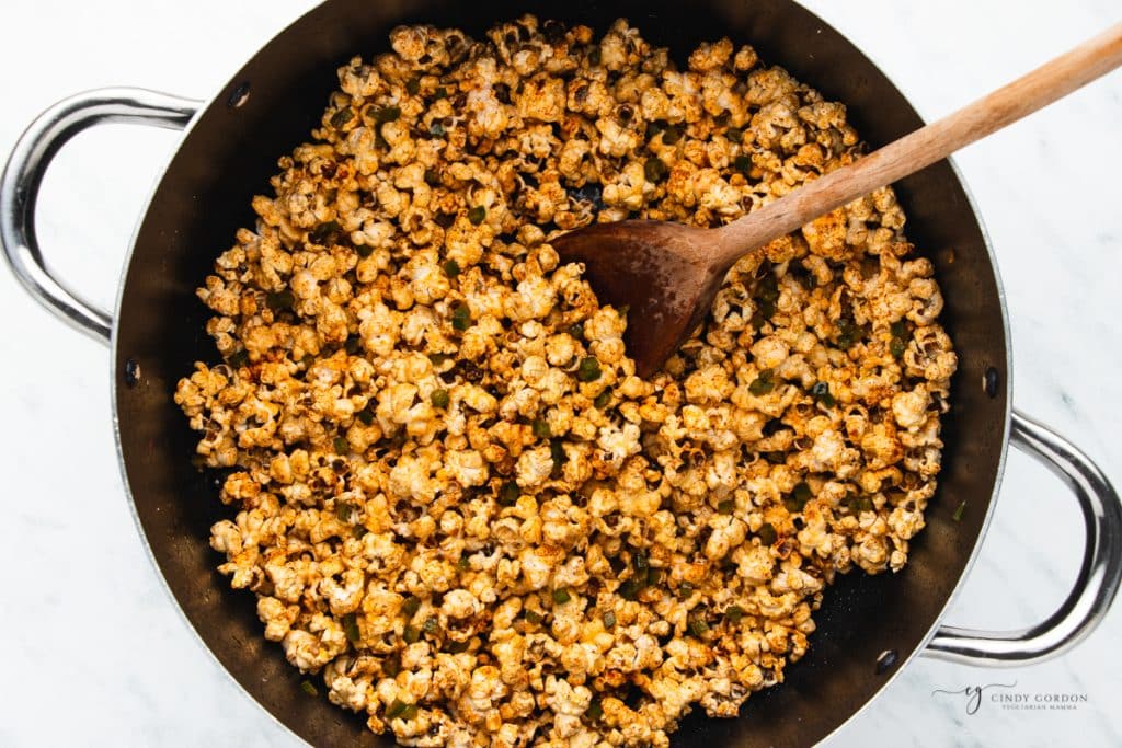 popcorn in a pot, coated with chili powder and butter, stirred with a wooden spoon.