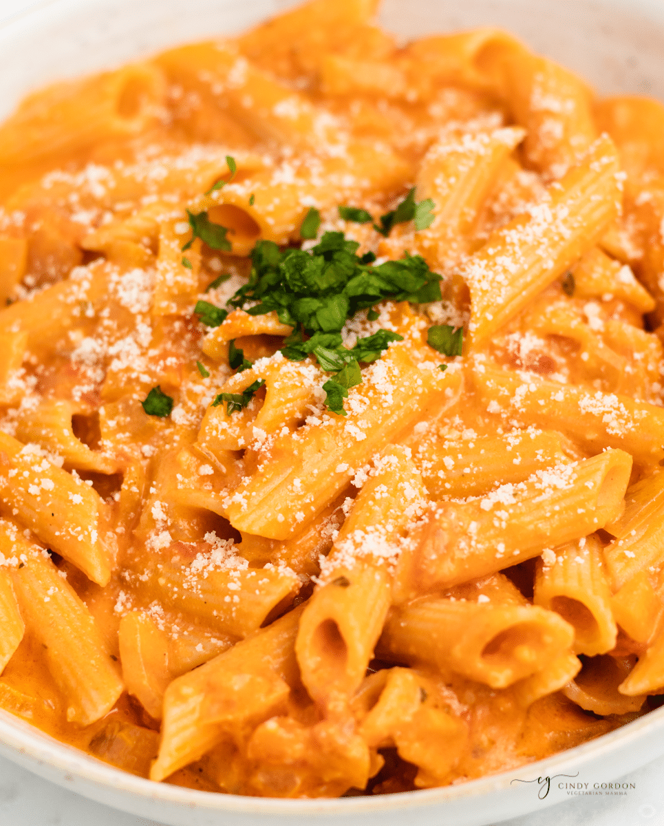 penne pasta with palomino sauce in a bowl, topped with parmesan and parsley. 