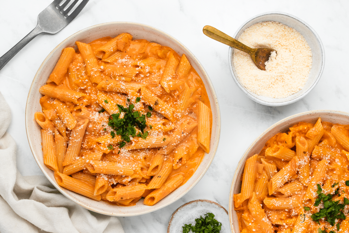 two bowls of palomino sauce on pasta, served with a small bowl of parmesan cheese. 