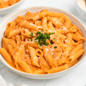 a bowl of penne pasta with palomino sauce in a bowl, topped with parmesan and parsley.