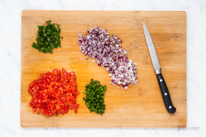 diced onion, tomato and jalapeno on a wooden cutting board along with a knife.