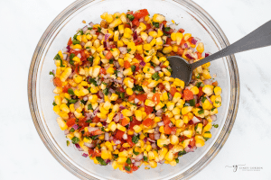 Roasted corn pico salsa in a clear glass bowl with a spoon