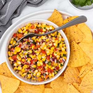 a white bowl of roasted corn pico on a plate of corn chips.