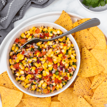 a white bowl of roasted corn pico on a plate of corn chips.