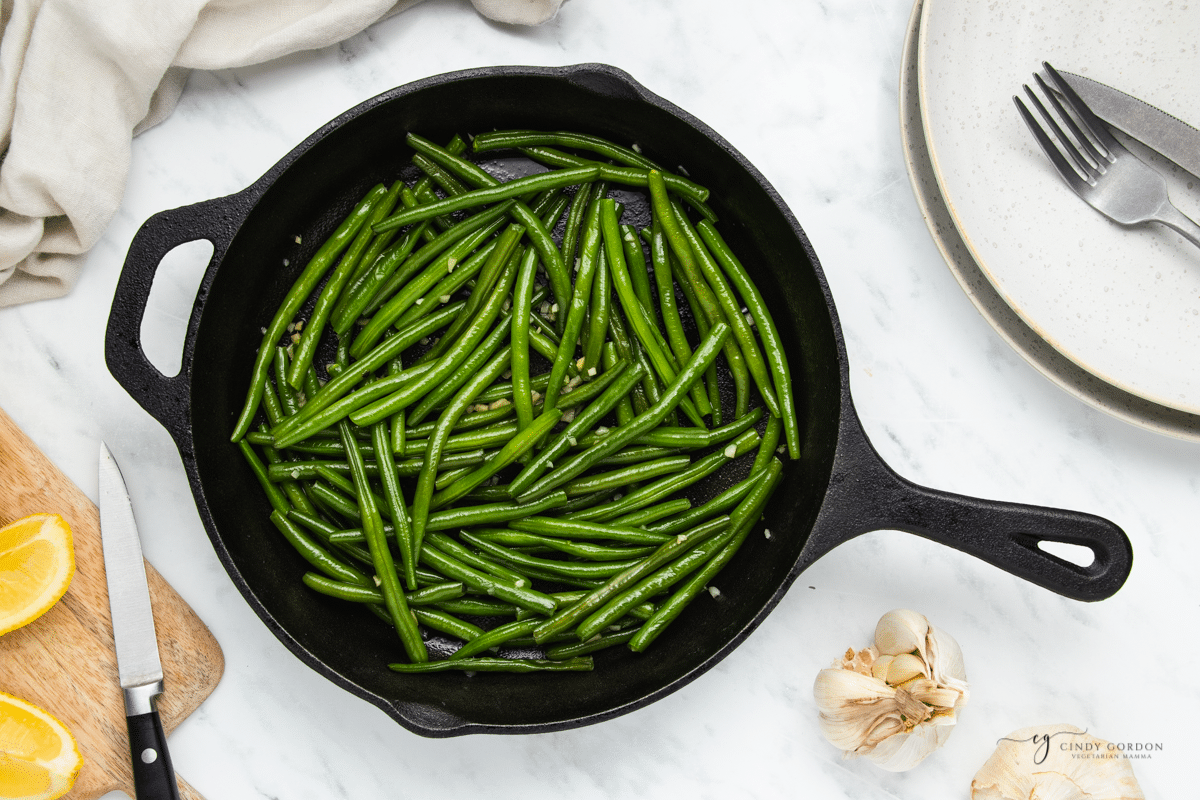 a black iron skillet of sauteed green beans with garlic. 