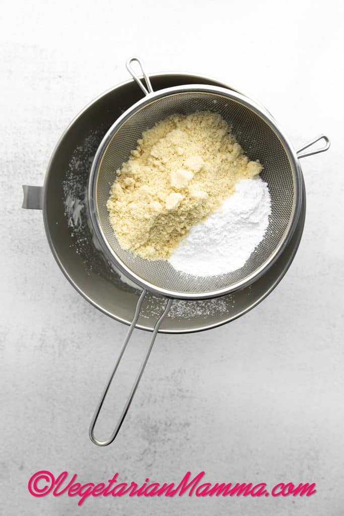 Add gel food coloring, if using. Then, sift the powdered sugar and almond flour into the egg whites using a fine-mesh sieve.