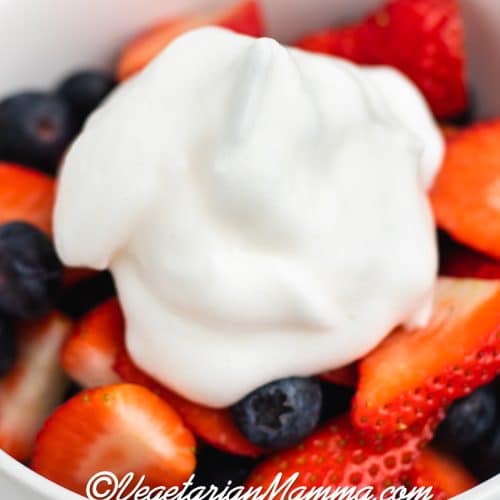 a white bowl of sliced strawberries and blueberries topped with a dollop of aquafaba whipped cream.