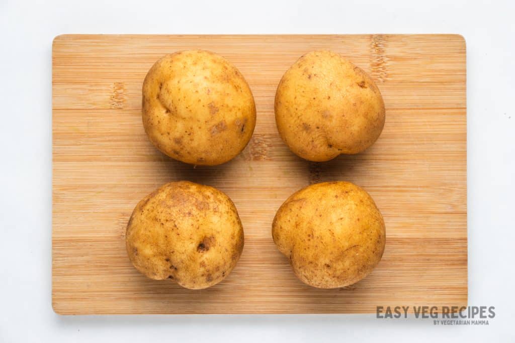 Four round potatoes on a wooden cutting board
