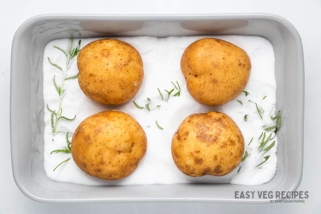 four potatoes in a baking pan filled with salt, sprinkled with rosemary.