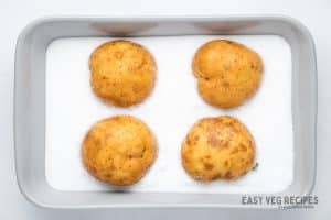 four potatoes in a metal baking pan of salt.