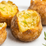 baked potatoes coated in salt, split open and sprinkled with rosemary.