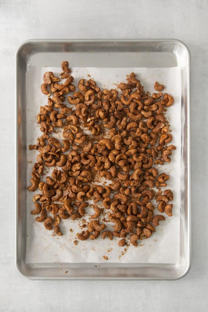 a baking tray lined with parchment, filled with cooked candied cashews.