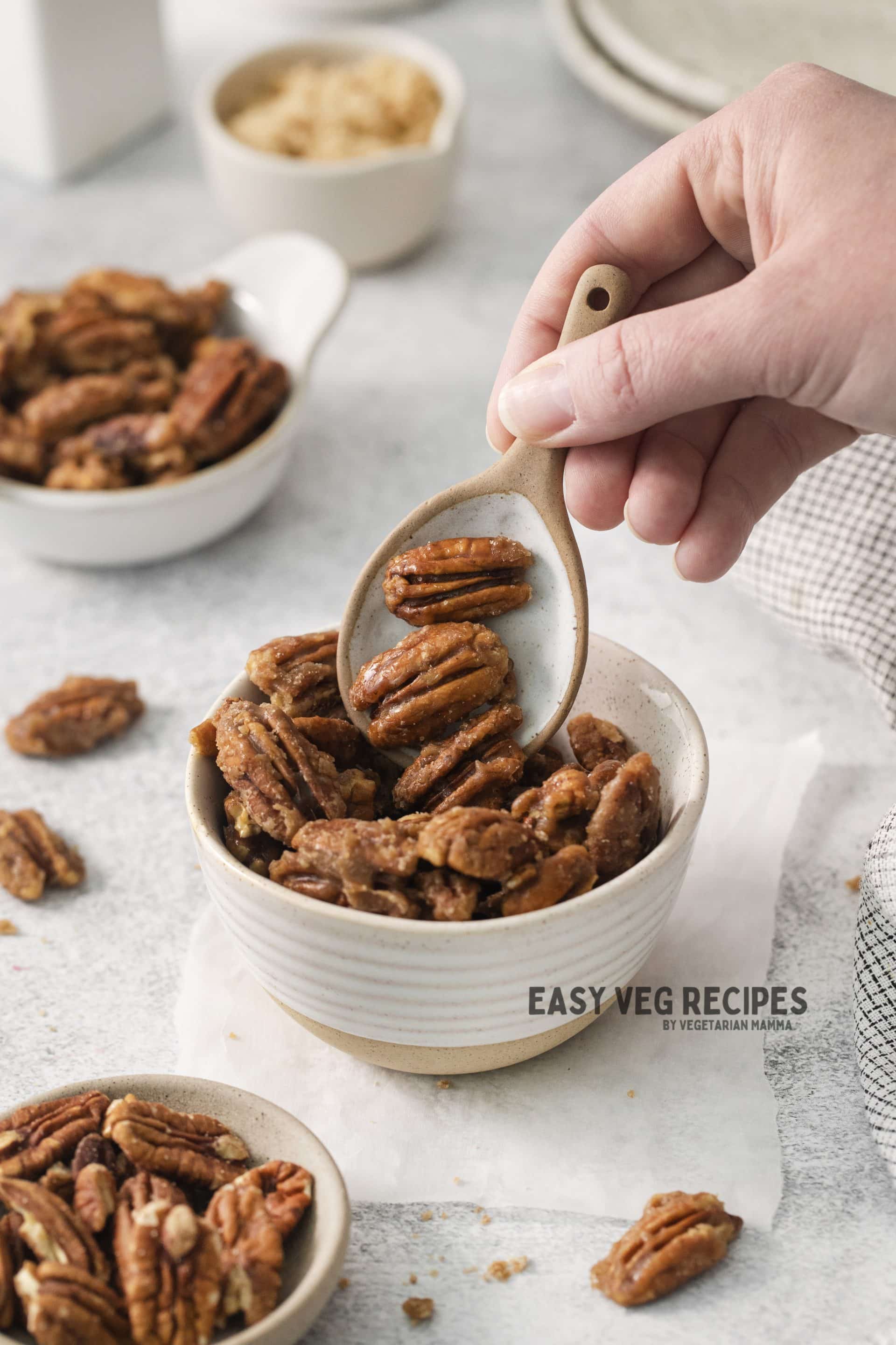 a bowl of candied pecans. A hand is using a wide spoon to pick some up. 