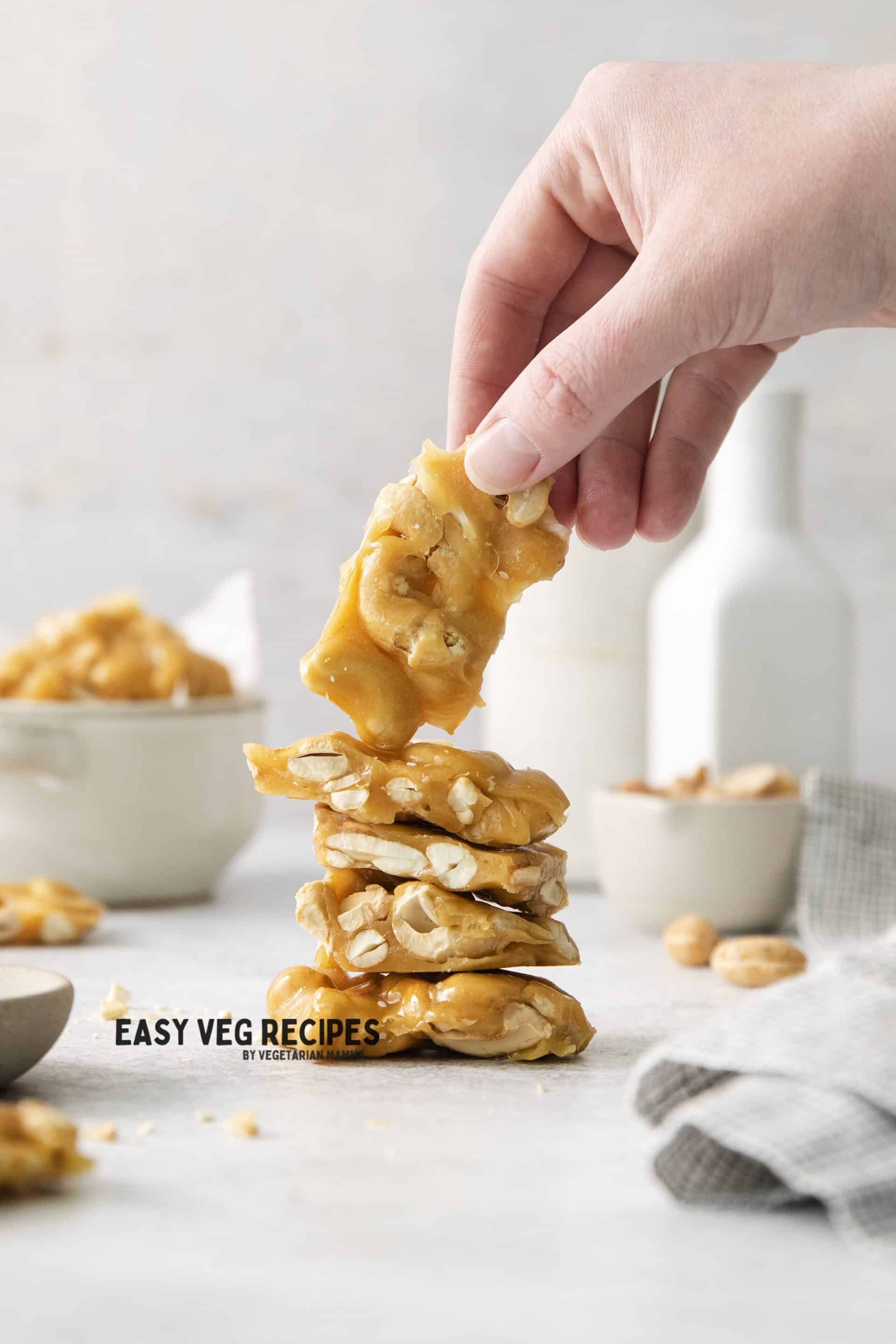 a hand picking up a rectangular piece of cashew brittle from a stack.
