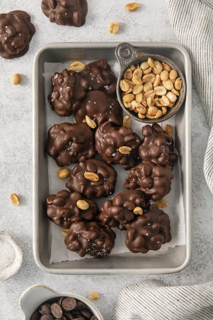 a sheet pan of peanut cluster candy with a small bowl of peanuts.