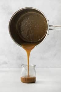 caramel sauce poured from a saucepan into a jar.