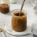 A small jar of dark homemade vegan caramel sauce with a spoon in it.