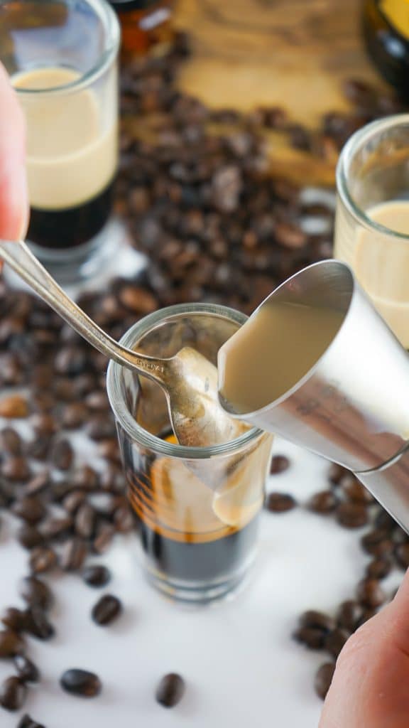 baileys poured over a spoon so that it will sit on top of kahlua in a shot glass.