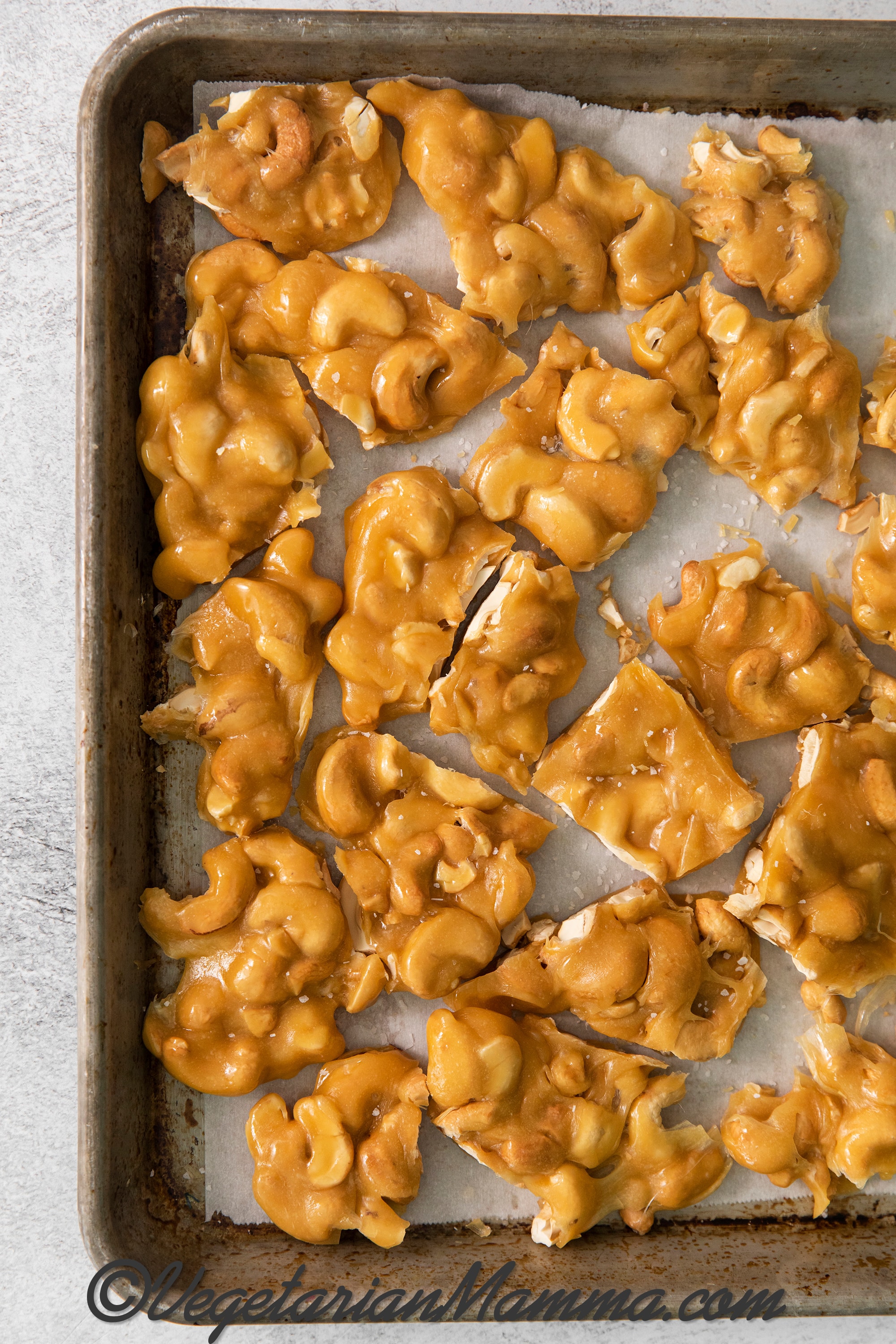 cashew brittle broken up into pieces on a parchment-lined baking sheet