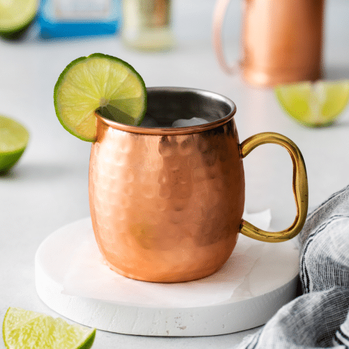 a copper mug filled with ice and london mule. A lime wheel garnishes the mug.