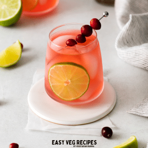 a white coaster holding a glass of cosmos on the rocks garnished with lime and cranberry.